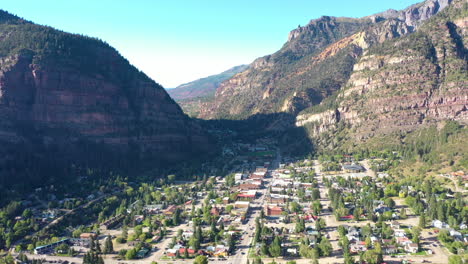Aerial-Drone-Footage-of-Ouray-Colorado-Mountain-City,-Cars-Driving-Through-Downtown-and-Houses-Surrounded-by-Rocky-Mountain-Cliffs-and-Shadow-Cast-Across-Town