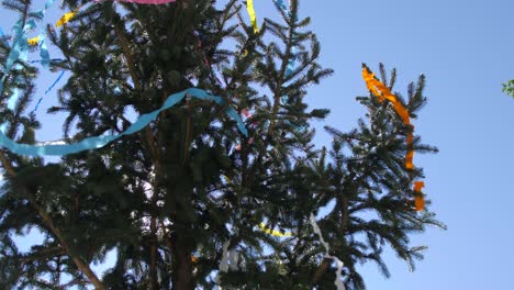 spruce-tree-decorated-with-paper-belts-and-ribbons,-blue-sky-in-background,-pan