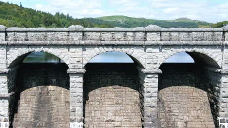 Rising-Aerial-Reveal-of-Burrator-Reservoir-Beyond-Stone-Dam-with-Car-Driving-By