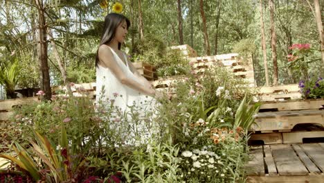 A-beautiful-Asian-woman-in-a-flowing-white-gown-looks-out-over-an-idyllic-flower-garden