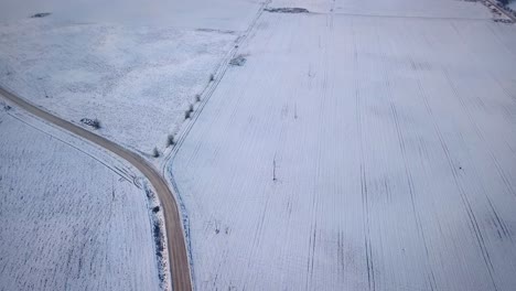 Empty-Road-And-Snowy-Field-In-Latvia-During-Winter---aerial-tilt-up