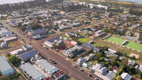 Port-Fairy-city-with-buildings,soccer-field-and-beautiful-reflected-ocean-in-the-background,-Aerial-backwards-shot