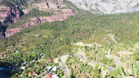 Aerial-Drone-Rising-Motion-of-Beautiful-Ouray-Colorado-Pine-Tree-Forest-and-Mountain-Cliffs-with-Cars-Driving-on-Highway-550-by-Rocky-Mountain-Houses