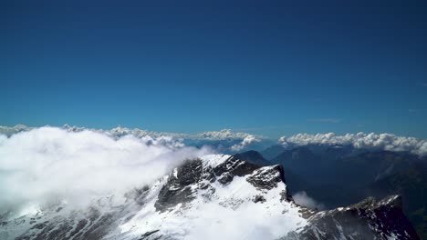 Clouds-Crawling-along-Jagged-Mountain-Range-with-Snow-on-Summit