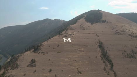 People-hiking-on-the-white-University-M-logo-on-the-mountains-of-Montana--aerial