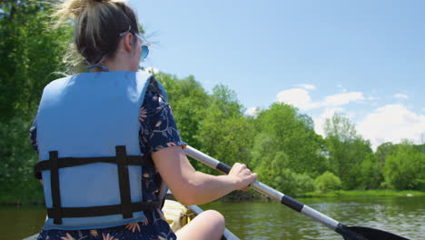 Stylish-young-woman-leisurely-rowing-a-canoe-down-a-river