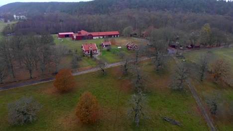 Aerial-view-of-land-with-red-farm-houses-surrounded-by-trees,-arc-shot