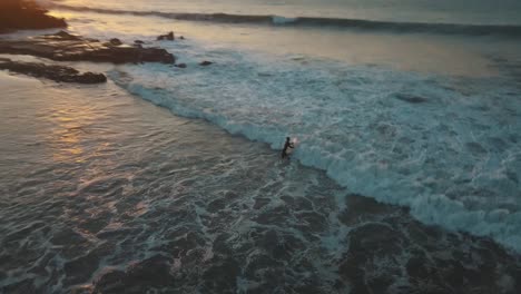 Surfer-dives-in-sea-at-sunset-with-wave-breaking-on-beach,-Peru