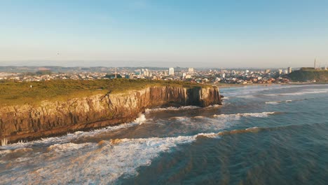 Epic-aerial-view-near-high-cliffs-beach-and-city-skyline-by-the-ocean-at-sunrise