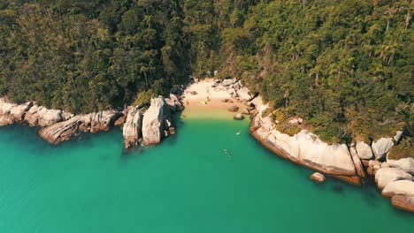 Aerial-view-approaching-a-brazilian-secret-paradise-beach-with-turquoise-color-water-located-in-Bombinhas,-Santa-Catarina,-Brazil