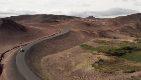 Car-travels-on-scenic-road-in-dry-barren-landscape-of-Iceland,-aerial