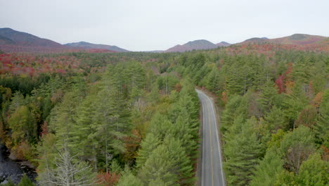 Slow-Rising-Aerial-View-of-an-Empty-Highway-Cutting-Through-a-Vast-Forest-in-the-Adirondack-Mountains-with-Vibrant-Fall-Colors