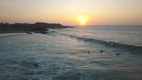 Beautiful-Golden-Hour-Sunset-By-The-Ocean-In-Lobitos,-Peru-With-Surfers-Waiting-For-Waves-In-The-Water