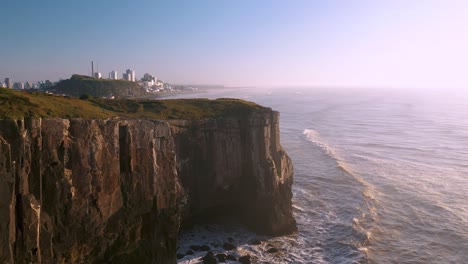 Drone-aerial-cinematic-shot-of-high-rocky-cliffs-on-atlantic-ocean,-located-in-Torres,-Rio-Grande-Do-Sul,-Brazil