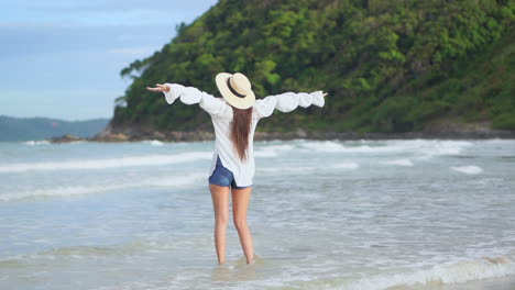 Young-woman-on-seashore-expresses-freedom-concept-by-raising-arms-to-the-sky
