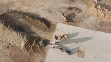 Loader-And-Dump-Truck-At-Work-In-A-Construction-Site-On-A-Sunny-Morning---aerial-top-down,-static-shot