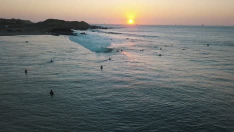 Drone-aerial-view,-Sunset-on-the-pacific-ocean-and-surfers-waiting-for-the-waves-by-the-coastline-in-Peru