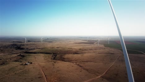 Super-wide-aerial-pull-back-of-the-Texas-horizon-on-a-wind-farm-close-to-the-propellers-of-a-wind-turbine