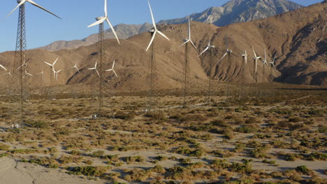 Stunning-aerial-view-of-drone-rotating-around-many-wind-turbines-with-huge-mountain-in-the-background-at-wind-farm-near-Palm-Springs-in-the-Mojave-Desert,-California,-USA