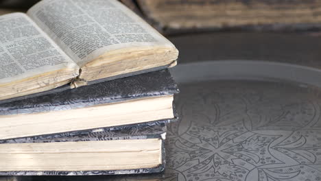 Close-up-tilt-of-old-used-books-on-decorated-metal-tray-on-table