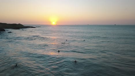 Drohnenluftaufnahme-Ein-Wunderschöner-Sonnenuntergang-Am-Pazifischen-Ozean-Und-Surfer,-Die-Auf-Die-Wellen-An-Der-Küste-In-Peru-Warten