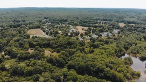 Descending-drone-shot-of-a-forest-around-a-small-town-in-Massachusetts-with-a-cloudy-sky-overhead---4K