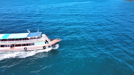 Aerial-4k-drone-footage-circling-a-fast-moving-ferryboat-with-passengers-bound-for-the-exotic-resort-of-Ko-Larn,-Thailand