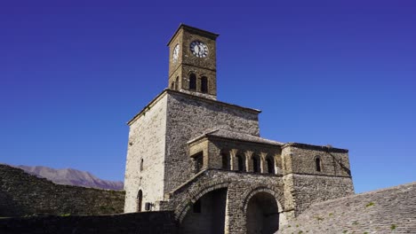 Medieval-clock-tower-surrounded-stone-walls-on-bright-blue-sky-background-in-Gjirokastra