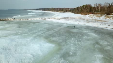 Aerial-of-People-Walking-on-Ice,-Half-Frozen-Sea-Shore---Dolly-out-Drone-shot