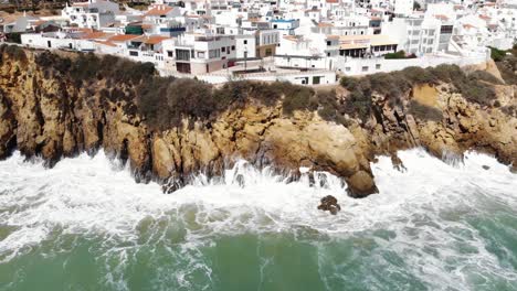 Aerial-4k-drone-footage-pulling-back-to-reveal-ocean-waves-crashing-against-the-rocky-cliffs-of-the-seaside-resort-town-of-Albufeira,-Portugal