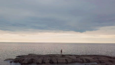 Man-celebrates-with-elation-standing-on-rocks-looking-out-to-empty-sea-horizon