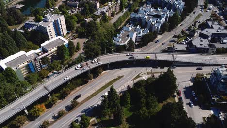 aerial-hold-above-overpass-no-traffic-on-all-lanes-birds-view-low-rise-apartments-tall-trees-white-sedans-crossing-tailed-by-a-black-suv-a-yellow-taxi-van-consutruction-vehicles-parked-on-shoulder-1-5