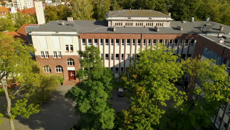 Facultad-De-Administración-De-La-Universidad-De-Gdansk,-Edificio-Antiguo-De-Arquitectura-Histórica-De-Ladrillo-Rojo-Y-árbol-Alto-Verde-En-El-Estacionamiento