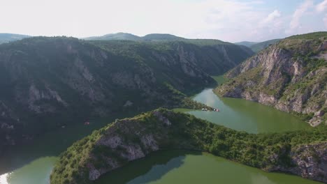 Mittlere-Höhe-Des-Mäandrierenden-Flusses-Uvac-In-Europa-Serbien-Mit-Kleinen-Gebäuden-Und-Einem-Boot-Am-Grünen-Wasser,-Luft-Vorwärts-Langsam