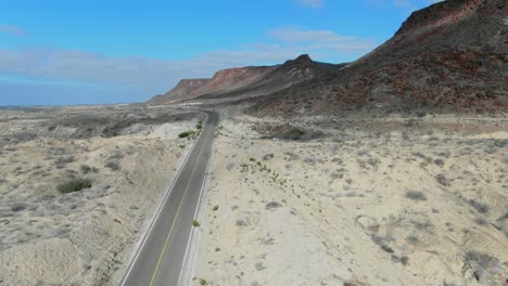 Aerial-view-moving-forward-shot,-highway-besides-a-red-rocky-mountain-in-La-Purisima-Baja-California-sur,-Mexico,-blue-sky-in-the-background