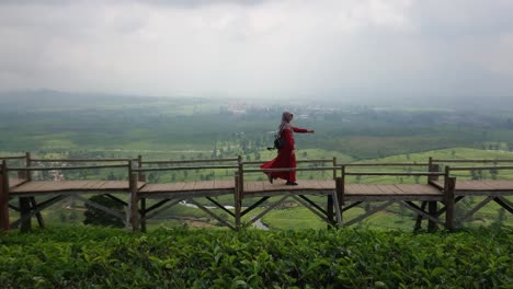 Happy-young-woman-wearing-muslim-dress-walking-on-wooden-bridge-with-beautiful-view-of-nature-in-the-tea-plantations