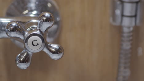 Hand-turns-handle-for-cold-water-in-shower,-close-up