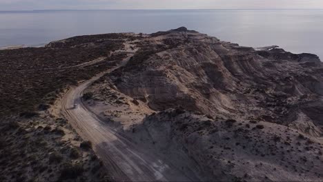 Car-driving-on-a-desert-road-near-the-sea-in-Patagonia---Aerial-tracking-shot