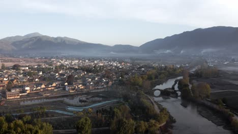 Schönes-Altes-Chinesisches-Dorf-Und-Steinbogenbrücke-über-Den-Fluss,-Luftbild