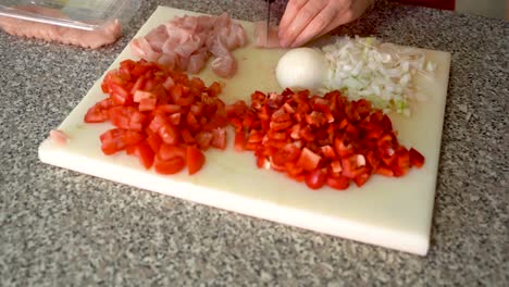 Close-up-on-hands-cutting-chicken-on-cutting-board-next-to-red-vegetables