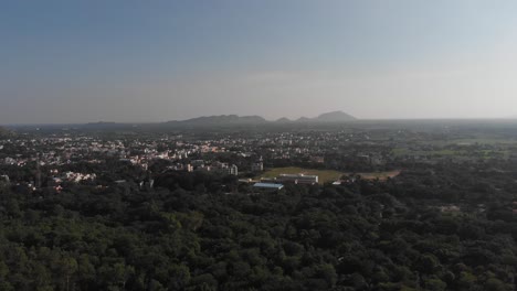 Descending-aerial-shot-of-green-forest-and-Tiruvannamalai-City-in-background-during-beautiful-day-in-nature,wide-shot