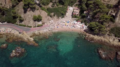 Tiny-beach-with-boats-and-tourists-sunbathing-and-swimming-in-Lloret-de-Mar-from-above