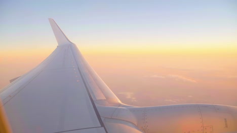 Blick-Aus-Dem-Fenster-Eines-Flugzeugflügels-Mit-Sanft-Pastellfarbenem-Sonnenuntergang-In-Den-Wolken