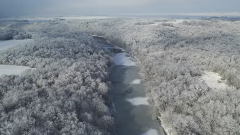 Frozen-River-Reveals-Vast-Snow-Covered-Forest,-Tilt-up-Aerial