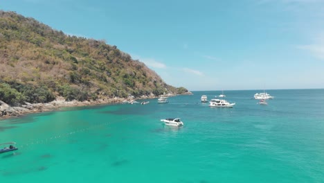 Yachts-and-Crystal-clear-blue-waters-surrounding-the-steep-hill-bordering-the-shore-in-Ko-Racha-Yai-Island-in-Thailand---Aerial-Low-angle-Panoramic-shot