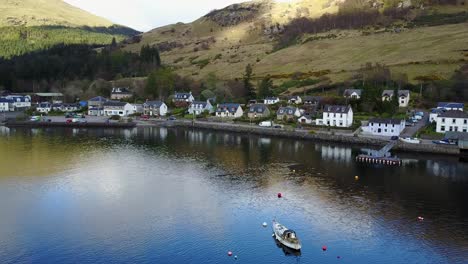 Village-of-Lochgoilhead-aerial-pan-revealing-a-sail-boat-in-the-water,-Scottish-Highlands
