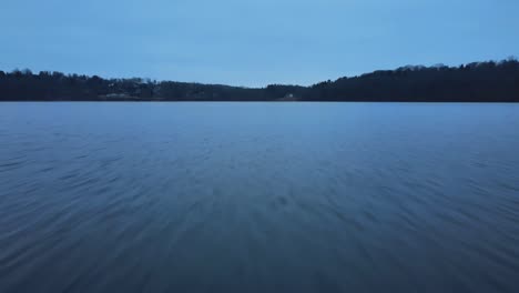 Drone-flying-close-to-the-water-on-a-lake-just-after-sunset-during-the-blue-hour-in-the-appalachian-mountains-during-winter