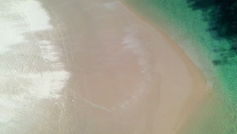 Downward-angle-drone-shot-of-the-of-wind-blowing-sand-across-a-sand-bar-at-Hat-Head-New-South-Wales,-Australia