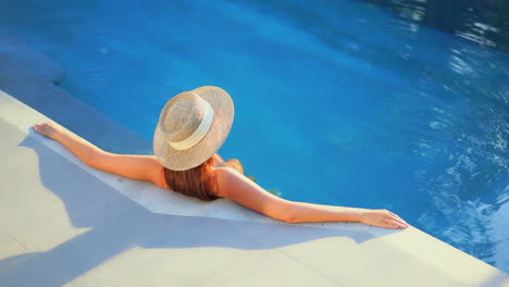 Back-view-of-woman-with-hat-sitting-in-pool-water