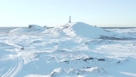 White-winter-landscape-at-Reykjanes-Lighthouse-on-hill-and-car-driving-on-road